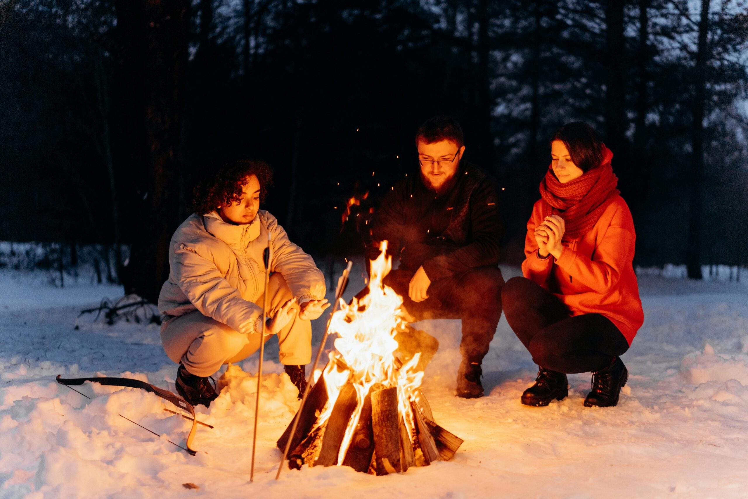 A glowing campfire at dusk surrounded by snowy pines