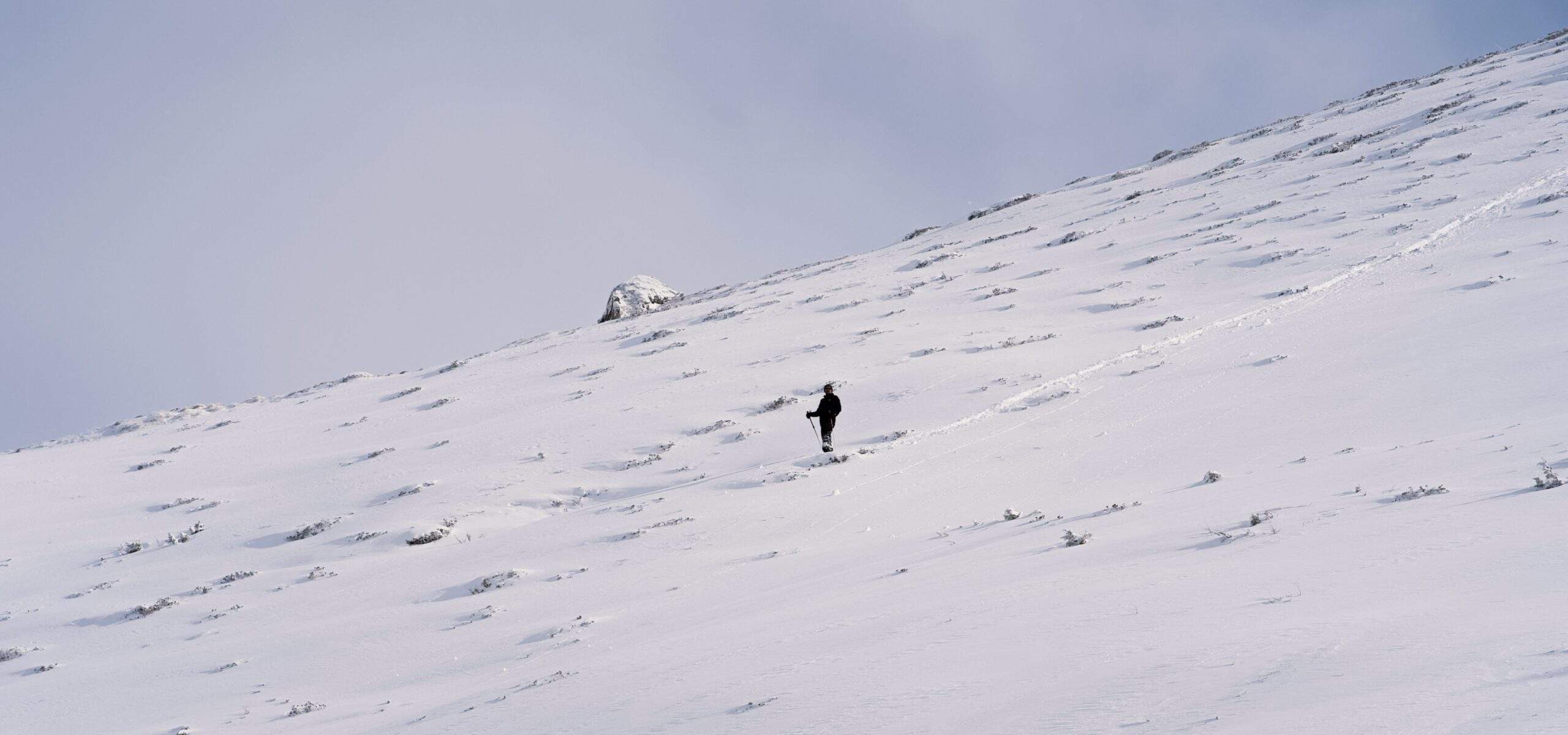 A lone hiker struggling uphill in deep snow with heavy backpack